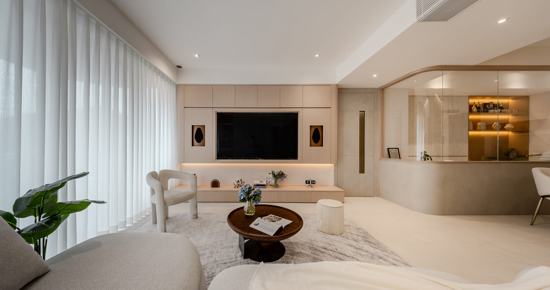 ED Design Fulham Garden 住宅案例，奶油米白客廳設有弧形開放式吧枱、整合電視牆與暖色展示櫃